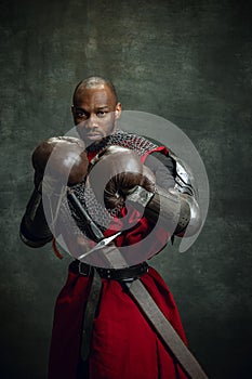 Vintage style portrait of brutal dark skinned man, medieval warrior or knight wearing armour in boxing gloves isolated