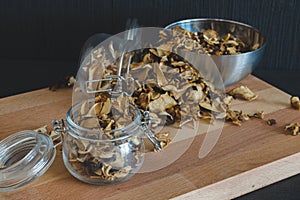 Vintage styled photo of sliced, chopped and dried various mushrooms in preserving glass and silver bowl standing on wooden desk o