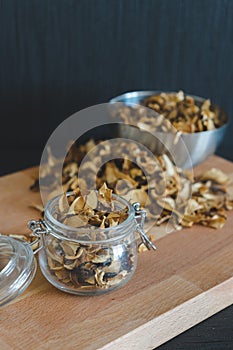 Vintage styled vertical photo of sliced, chopped and dried various mushrooms in preserving glass and silver bowl standing on wood