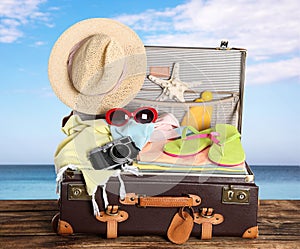 Vintage suitcase packed for summer vacation on wooden surface against sea