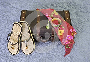 Vintage suitcase with sandals, bracelet, scarf and necklace draped on it, tropic travel concept