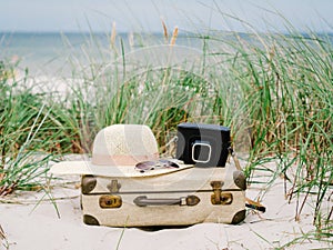 Vintage suitcase, summer hat, and a retro photo camera in the dunes