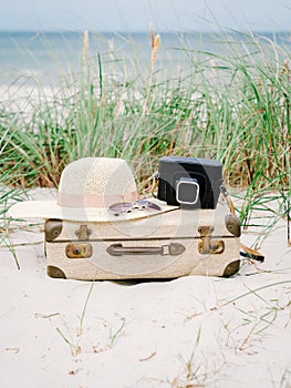 Vintage suitcase, summer hat, and a retro photo camera in the dunes