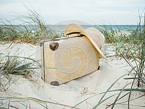 Vintage suitcase, summer hat, and a retro photo camera in the dunes