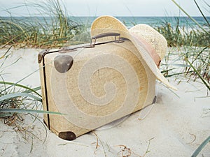 Vintage suitcase, summer hat, and a retro photo camera in the dunes