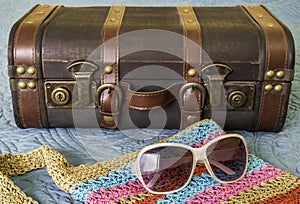 Vintage suitcase, sunglasses and woven colorful purse on bed, pa