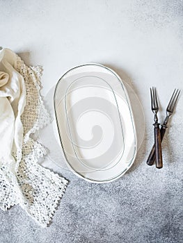 Vintage table setting with oval plate, white lace napkin and forks on a grey background. Top view. Copy space