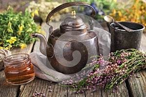 Vintage teapot, cup of herbal tea, honey jar, medicinal herbs bunches on background. photo