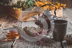 Vintage teapot, cup of herbal tea, honey jar, heather bunch and medicinal herbs on background.