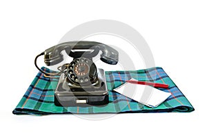 Vintage telephone on tartan plaid with red pen and notepad with copyspace