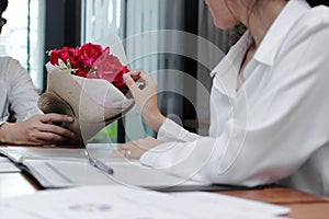 Vintage toned image of attractive young Asian woman accepting a bouquet of red roses from boyfriend in office on valentine`s day.