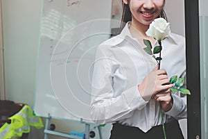 Vintage toned image of cheerful young Asian business woman holding a white roses in office on Valentine`s day. Love and romance i