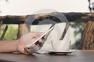 Vintage toned image of coffee cup with hands of young man holding mobile phone in nature background. Selective focus and shallow d