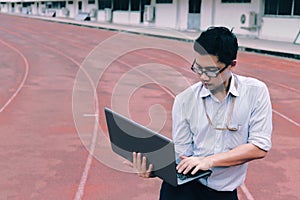 Vintage toned image of professional young Asian businessman with laptop standing on race track. business vision concept