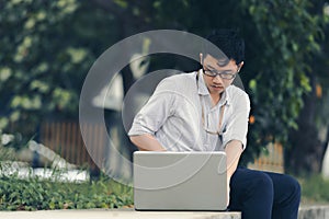 Vintage toned image of relaxed young Asian business man working with laptop at public park.