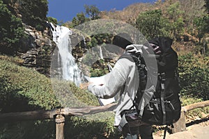 Vintage toned image of young Asian backpacker looking map on his hands in waterfall national park.