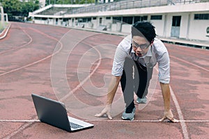 Vintage toned image of young Asian businessman with laptop ready start position to forward on race track. Competition and vision b