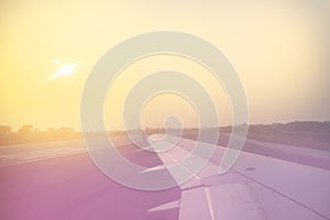 Vintage toned plane wing above runway at sunrise