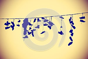 Vintage toned silhouettes of shoes hanging on cable.