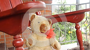 A vintage toy bear sits and sways in a rocking chair on an open veranda. Summer greens.