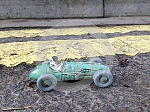 Vintage toy racing car & driver close up with worn green patina, in front of double yellow line no parking restriction.