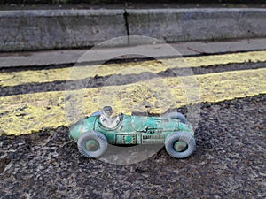 Vintage toy racing car & driver with worn green patina, in front of double yellow line no parking restriction.