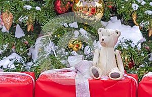 Vintage toy teddy bear near a snowy Christmas tree with gifts.