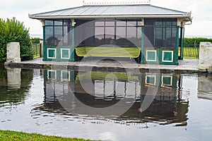 Vintage traditional shelter reflecting in a large puddle caused by rain and blacked drains on the west cliff promenade in Ramsgate