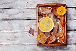 Vintage tray with autumn pumpkin soup decorated sesame seeds and thyme leaf in white bowl on rustic wooden table top view.