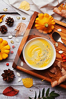 Vintage tray with warm autumn pumpkin soup decorated seeds and thyme in white bowl on rustic wooden table top view.