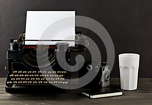 Vintage typewriter with empty, blank sheet of paper, camera, cup