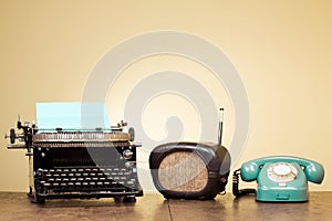 Vintage typewriter, old radio, retro telephone on wooden table front blue background. Vintage style photo