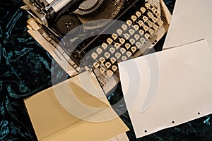 vintage typewriter on a piece of newspaper and dark blue velvet fabric on the floor with paper in it and other sheets of paper aro