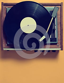 Vintage vinyl turntable with vinyl plate on a yellow pastel back.