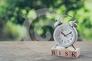 Vintage White Alarm Clock placed on wood word RISK. The concept of risk diversification of a business or organization. For the