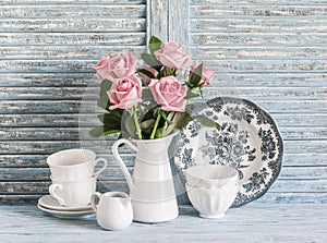 Vintage white crockery and rose bouquet on blue wooden background. Kitchen still life in vintage english country style. Flat lay