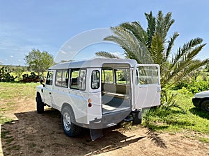 Vintage white landrover with rear doors open, blue skies and green foliage.