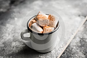 Vintage white metal cup with hot chocolate and marshmallow on the rustic background. Hygge winter evening. Selective focus.