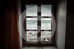 Vintage window with dramatic sea view with big stormy waves and dramatic overcast sky during rain and storm weather in fall season