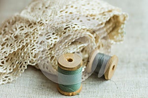Vintage wood spools with green and grey threads on linen fabric, cotton lace, sewing hobby concept