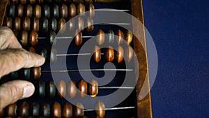 Vintage wooden abacus close up. A man s hand moves wooden knuckles on the bills. Part of the old end of the abacus on a dark blue