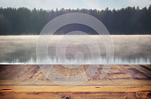 vintage wooden board table in front of abstract photo of misty and foggy lake at morning/evening.