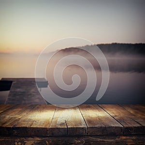 Vintage wooden board table in front of abstract photo of misty and foggy lake at morning sunrise.