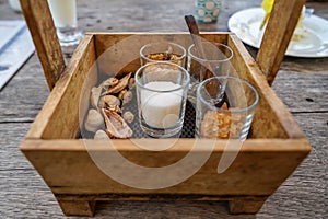 Vintage wooden box basket holding sugar glasses and spoon for coffee and tea with sea shell decoration on wooden table