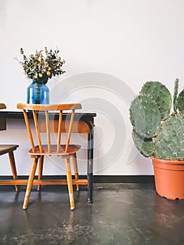 Vintage wooden elementary school desk with two wooden chairs, a dried flower arrangement in a blue vase against a white wall