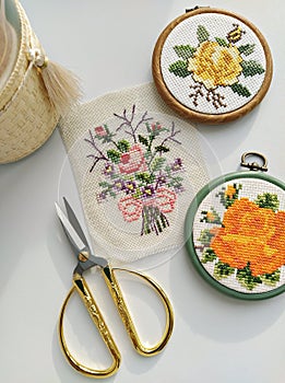 Vintage wooden embroidery hoops, scissors, needle, thread and fabric with floral cross-stitch embroidery on white