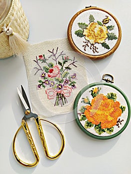 Vintage wooden embroidery hoops, scissors, needle, thread and fabric with floral cross-stitch embroidery on white