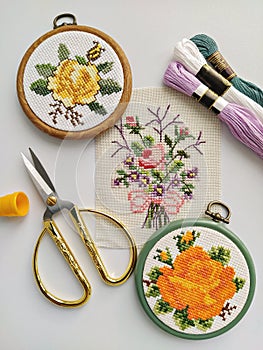 Vintage wooden embroidery hoops, scissors, needle, thread and fabric with floral cross-stitch embroidery on white