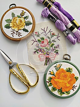Vintage wooden embroidery hoops, scissors, needle, thread and fabric with floral cross-stitch embroidery on white
