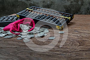 Vintage wooden hand abacus with pile of money coins from red cloth bag on rustic old wooden table